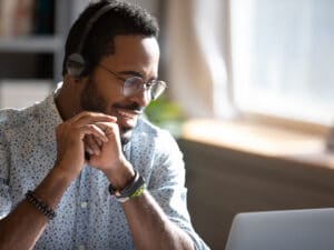 Smiling man wearing headphones speaking, using laptop