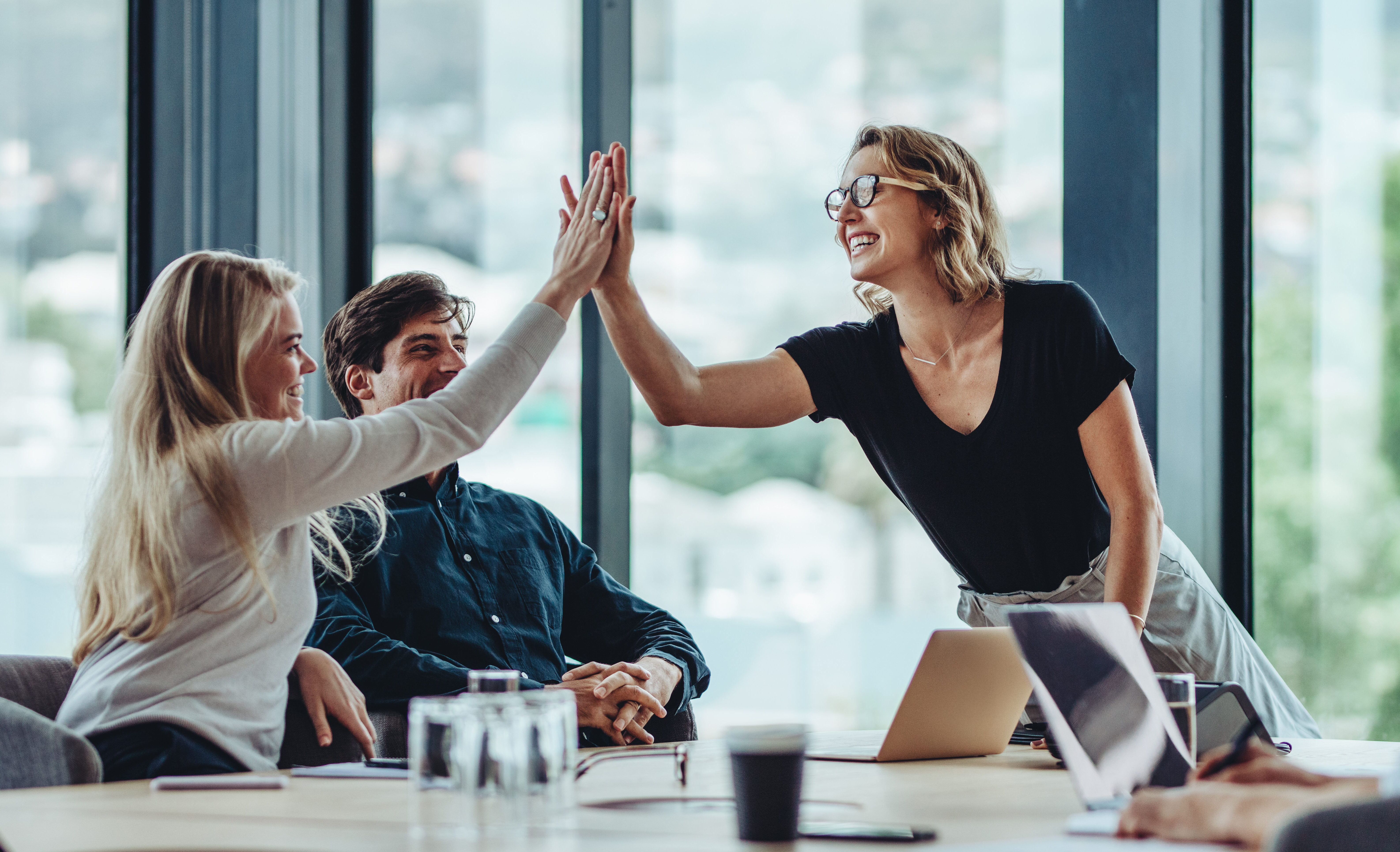 Female professional giving a high five to her colleague in conference room. Group of colleagues celebrating success in a meeting
