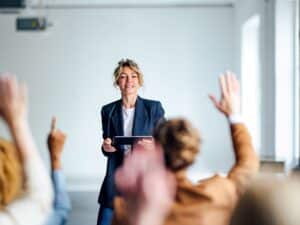 A women presents to a room of people with their hands up