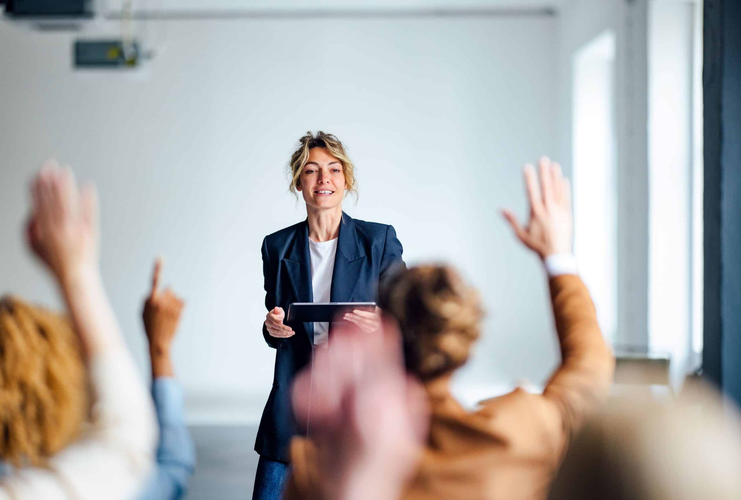 A women presents to a room of people with their hands up