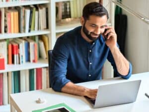 Smiling man on mobile, working from home on laptop