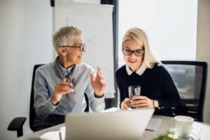 Young business woman looking at laptop when listening to mature coworker