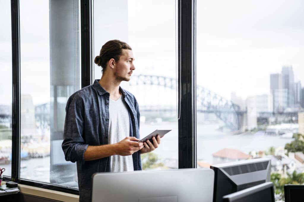 Casual young businessman with tablet by window in modern office