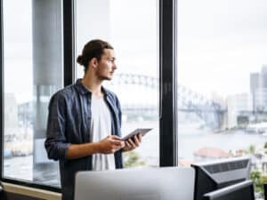Casual young businessman with tablet by window in modern office